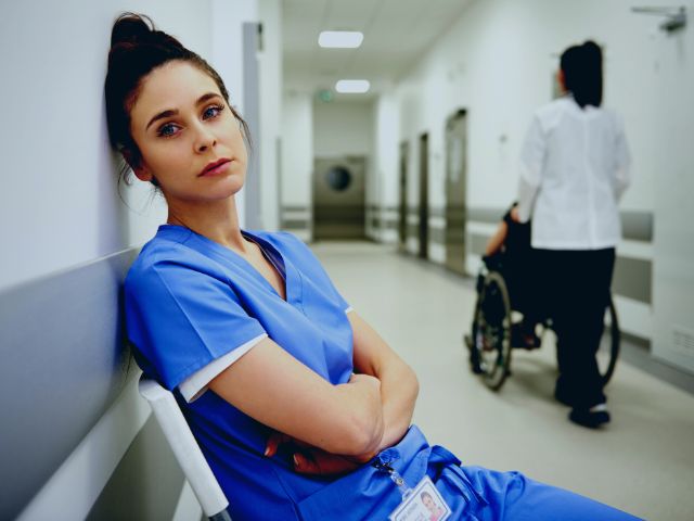 An exhausted baby nurse is leaning against the hospital wall.