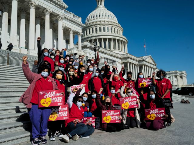 A group of nurses with their fists raised standing in front of the capital in support of the Safe Staffing Bill.