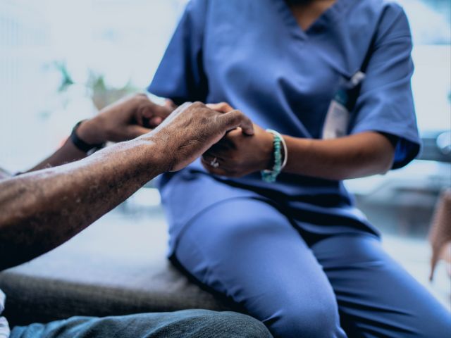 A geriatric nurse holding hands with her patient.