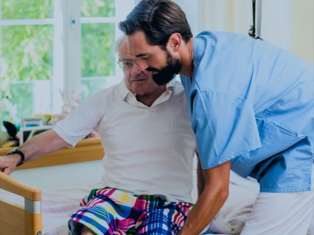 A geriatric nurse supporting his patient's legs to help him out of bed.