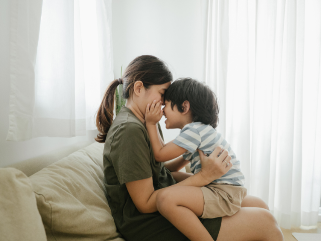 A mother sits on a couch with her child in her lap.